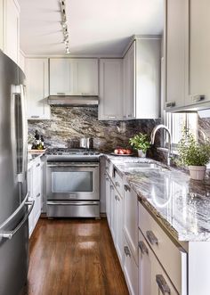 a kitchen with white cabinets and stainless steel appliances, wood flooring and marble counter tops