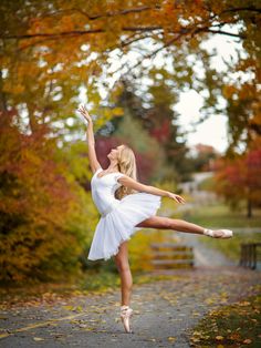 a young ballerina is posing in the fall leaves with her arms stretched out and legs spread wide