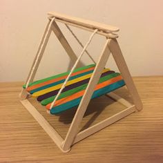 a wooden toy swing with multicolored stripes on the seat and back, sitting on a wood table