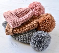 several knitted hats are stacked on top of each other, one with a pom - pom