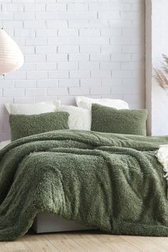 the comforter is green and has white pillows on it, along with a brick wall