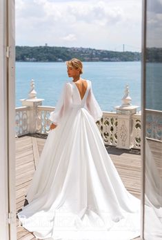 a woman in a white wedding dress standing on a deck looking out at the water