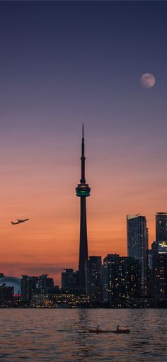 an airplane is flying over the city at night with a full moon in the sky