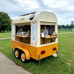 an orange and white food truck parked in the grass with a man behind it,