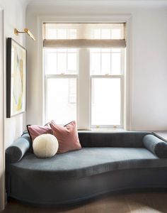 a black couch with two pillows on it in front of a window and some framed pictures