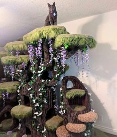 a cat sitting on top of a tree house made out of fake grass and flowers