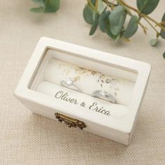 two wedding rings in a white box on a table next to some flowers and greenery