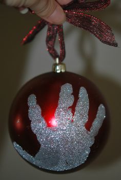 a handprinted ornament hanging from a red and silver ball with a ribbon