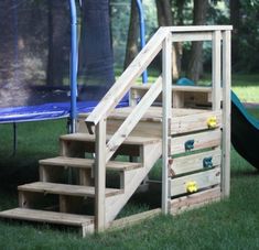 a set of stairs made out of pallets in the grass next to a blue trampoline