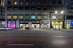 an empty street in front of a tall building at night with lights on the windows