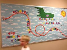 a young boy is standing in front of a bulletin board with a train on it