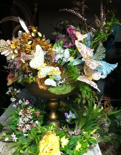 a vase filled with lots of flowers and butterflies on top of a table next to plants