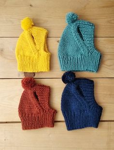 three knitted beanies with pom - poms sitting on top of a wooden floor