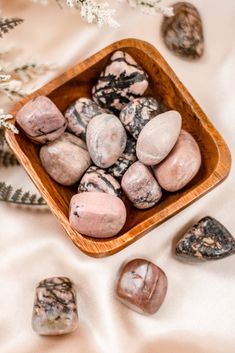 some rocks are in a wooden bowl on a white tablecloth with pine cones and branches