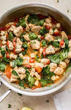 a pan filled with chicken, spinach and tomato soup next to a lemon wedge