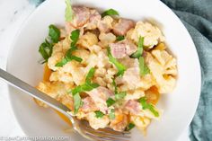 a white plate topped with macaroni and cheese covered in green leaves next to a fork