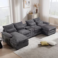 a living room with a large gray sectional couch and pillows on the floor, in front of a window