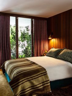 a large bed sitting in a bedroom next to a window with curtains on both sides