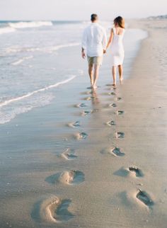 a man and woman walking on the beach with footprints in the sand as if they were holding hands