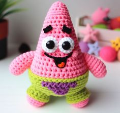 a pink crocheted toy with eyes and mouth, standing on a table next to other toys