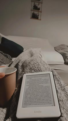 a kindle sitting on top of a bed next to a cup