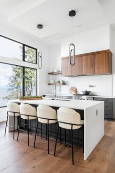 a kitchen with white counter tops and stools next to an open window that looks out onto the ocean