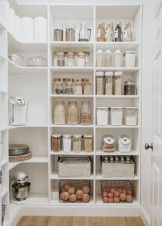 an organized pantry with lots of white shelves and baskets on the bottom shelf, filled with food