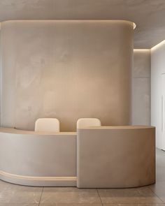 a curved counter in the middle of a room with two white chairs and a light colored wall behind it