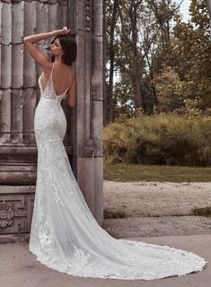 a woman in a wedding dress leaning against an old pillar with her back to the camera