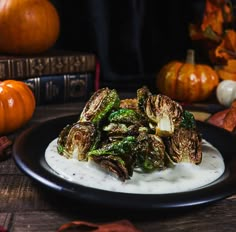 a black plate topped with brussel sprouts covered in white sauce next to pumpkins