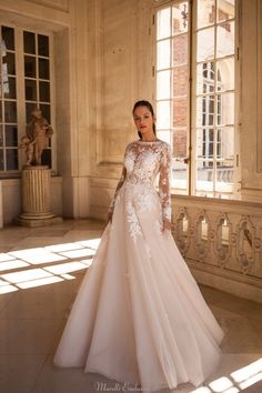 a woman in a wedding dress standing by a window