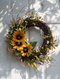 a wreath with sunflowers and greenery hanging on a white wooden door frame