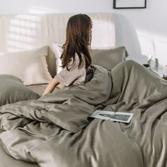 a woman sitting on top of a bed under a blanket