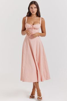 a woman is wearing a pink dress with straps and a bow on the waist,