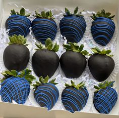 chocolate covered strawberries in a box with green leaves on the top and blue stripes