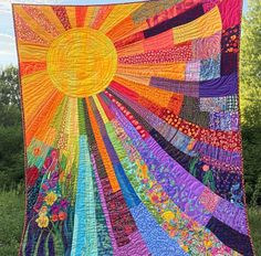 a large colorful quilt hanging from the side of a pole in front of some trees