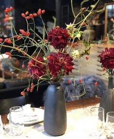 two vases filled with red flowers sitting on top of a white tablecloth covered table