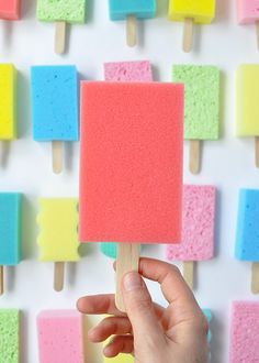 a hand is holding a popsicle with colored marshmallows on it in front of a wall