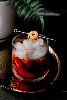 a glass filled with ice and an orange peel on top of a metal tray next to a potted plant