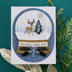 a handmade card with a deer and snow globe on it, surrounded by evergreen branches