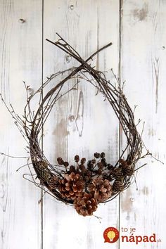 a wreath with pine cones and branches hanging on a white wooden wall next to scissors