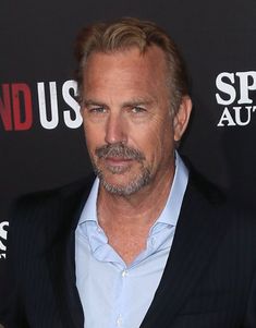 a man in a blue shirt and black blazer standing next to a red carpet