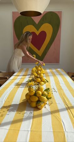 a woman reaching for flowers on a table with yellow and white striped cloth in front of a heart shaped painting