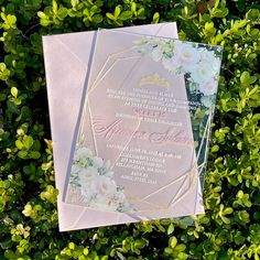 two wedding cards sitting on top of green bushes