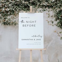 an easel with a sign that says welcome to the night before on it and greenery in the background