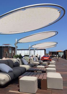 an outdoor seating area with couches, tables and umbrellas over looking the ocean