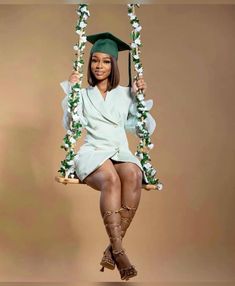 a woman in a graduation cap and gown sitting on a swing with flowers around her legs