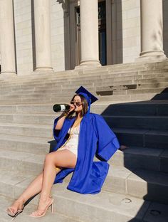 a woman in a graduation gown sitting on steps talking on her cell phone and drinking from a bottle