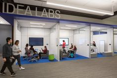 an office with people working on computers in the cubicle area, while others walk by