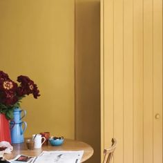 a table with flowers in vases and magazines on it next to a yellow wall